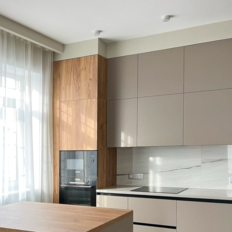 Virtuve pēc pasūtījuma Rīgā: apakšējās fasādes no krāsota matēta MDF, augšējās no EGGER lamināta, BLUM furnitūra un Tandembox atvilktnes, bezrokturu dizains un flīžu sienas panelis.